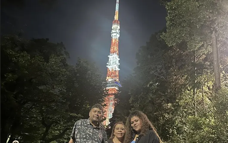 Three people taking a commemorative photo with Tokyo Tower in the background at night